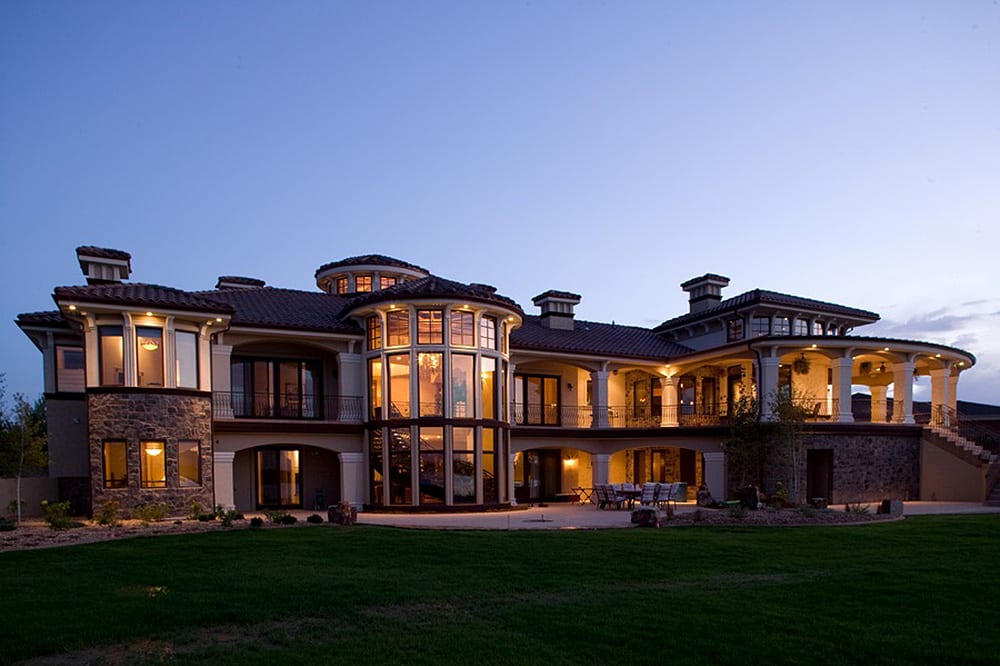 House plan exterior, two stories, featuring a curved colonnade, circular turret with extensive glazing, and stone accents.